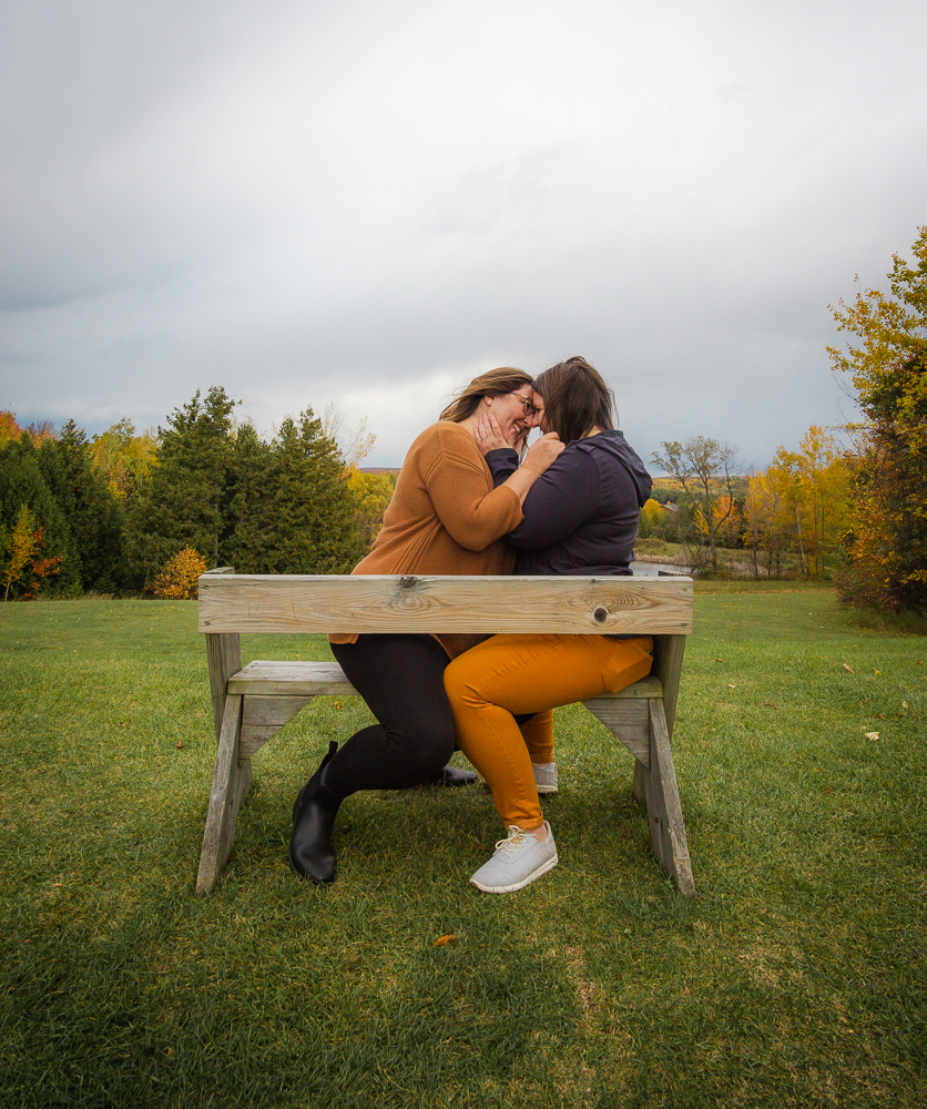 Lesbian couple kissing on park bench in fall