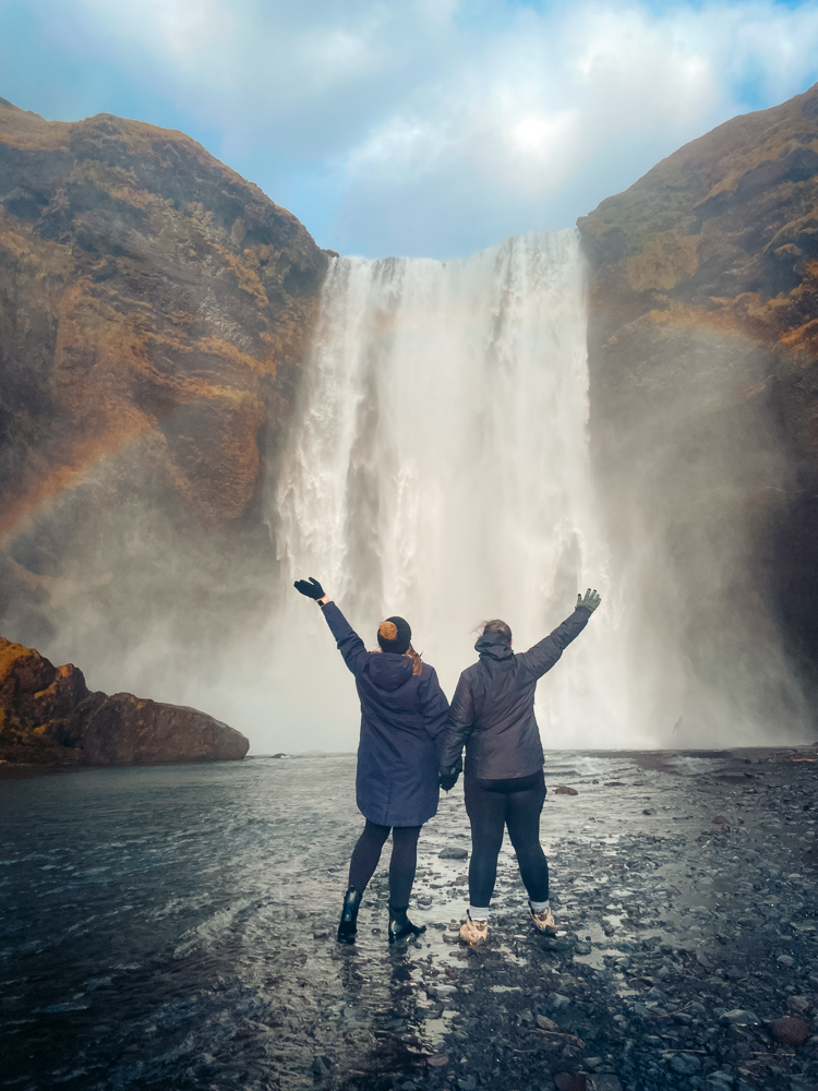 two women in front of large waterfall with rainbow