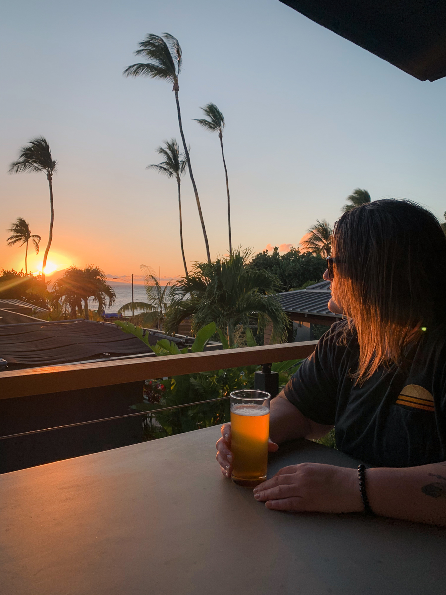 Girl on patio with beer watching sunset behind palm trees