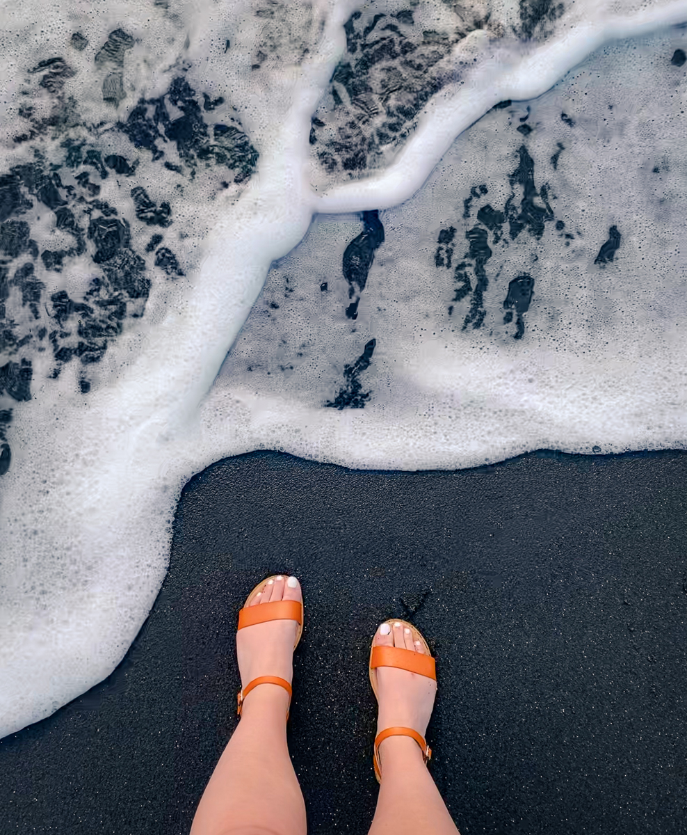 Sandaled feet on black sand beach at waianapanapa state park
